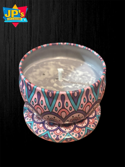 A small candle in a decorative tin with a colorful mandala pattern in pink, teal, purple, and orange, set against a black background with a JP's Gift and accessories logo in the top left corner.