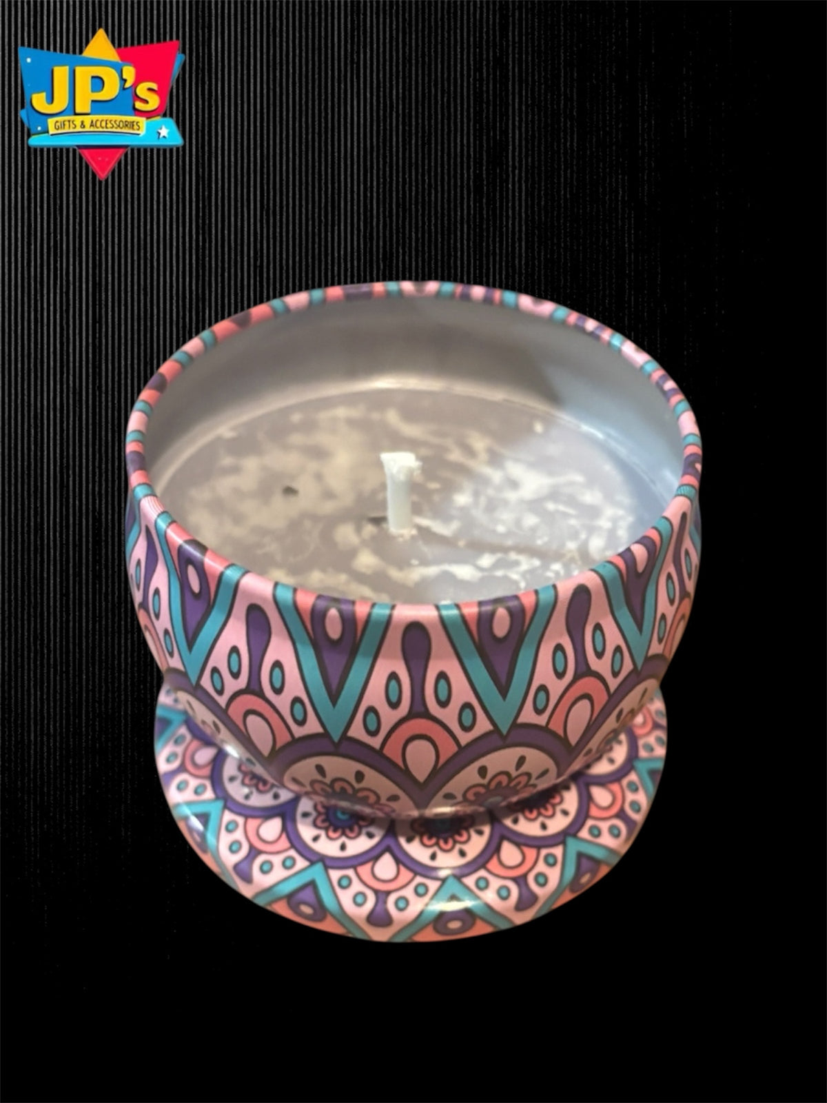 A small candle in a decorative tin with a colorful mandala pattern in pink, teal, purple, and orange, set against a black background with a JP's Gift and accessories logo in the top left corner.