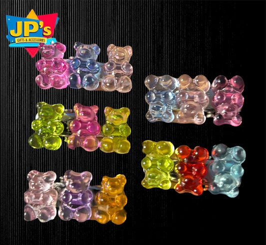 Nine colorful gummy bear-shaped hair clips in various colors including pink, blue, clear, yellow, purple, red, and green arranged on black background.
