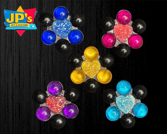 Five colorful funky fridge magnets with glitter centers and metallic spheres arranged on black striped background.